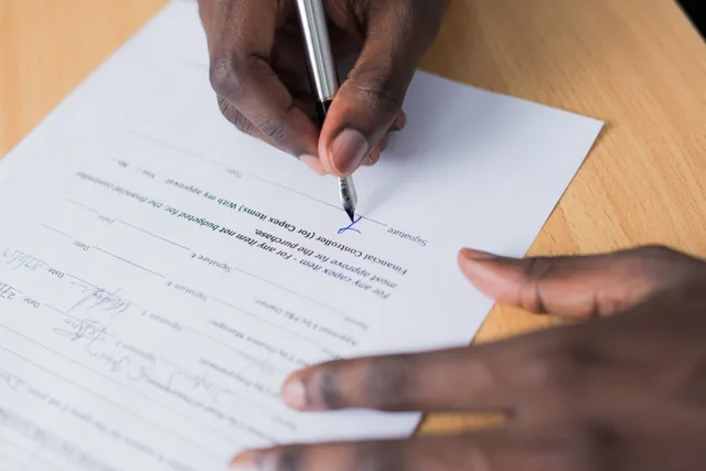 A close-up view of a person's hand signing a business contract on a desk with a pen. Media companies take fifteen different arrangement shapes, each documented